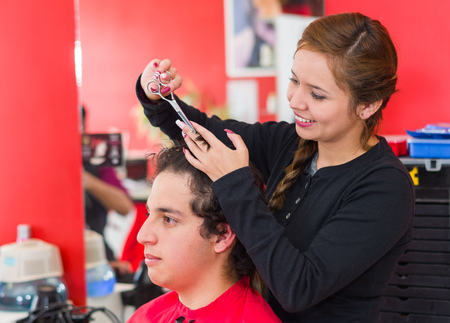 Inside a barbershop a young and nice hairstylists is cutting the hair of a man with curly hair.の写真素材