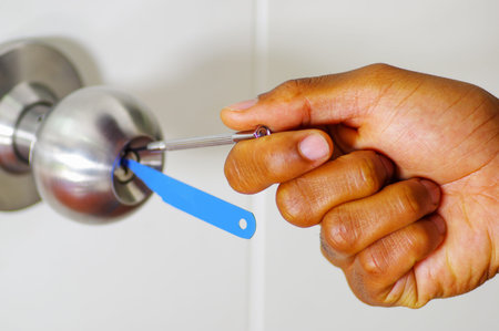 Closeup hands of locksmith using pick tools to open locked door.