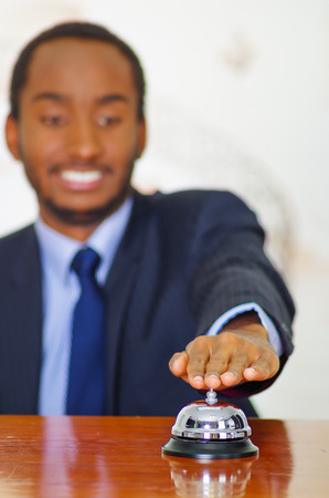 Man wearing elegant blue suit pressing desk bell at hotel reception.の写真素材
