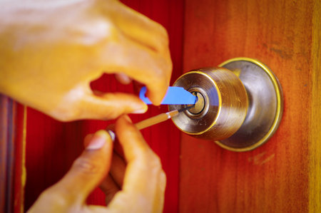 Closeup hands of locksmith using metal pick tools to open locked door.