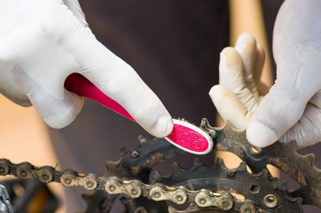 Closeup hand wearing white glove holding toothbrush rubbing on metal bicycle chain, mechanical repair concept.の写真素材