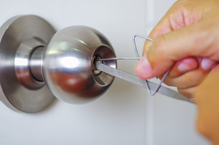 Closeup hands of locksmith using metal pick tools to open locked door.