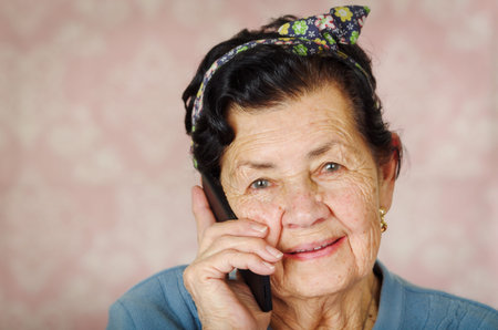 Older hispanic cute woman with flower pattern bow on her head wearing blue sweater in front of pink...