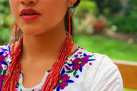 Closeup beautiful hispanic woman wearing traditional andean white blouse with colorful decoration around neck, matching red necklace, bracelet and ear ring.の写真素材