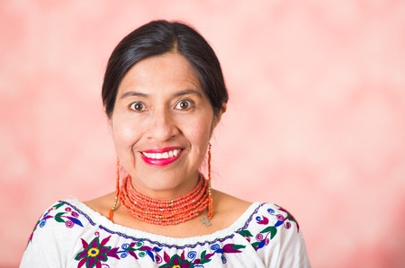 Headshot beautiful hispanic mother wearing traditional andean clothing, posing happily while smiling to camera, pink studio background.の写真素材