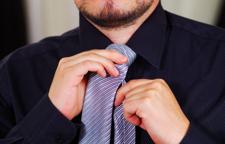 Closeup man's chest wearing white shirt, tying tie using hands, face partly visible, men getting dressed concept.の写真素材