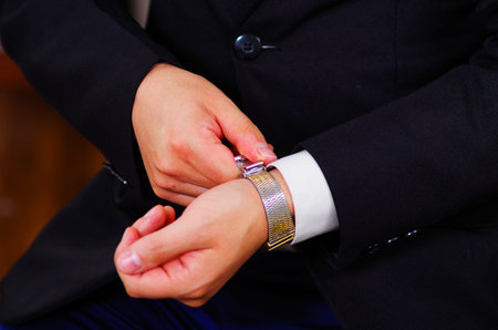 Closeup man's arm wearing suit, adjusting silver wrist watch using hands, men getting dressed concept.の写真素材