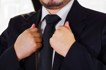Closeup man's chest area wearing formal suit and tie, adjusting jacket collar using hands, men getting dressed concept.の写真素材