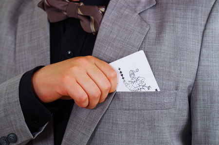 Closeup man's chest area wearing formal suit and tie, placing joker playing card in jacket pocket, men getting dressed concept.の写真素材