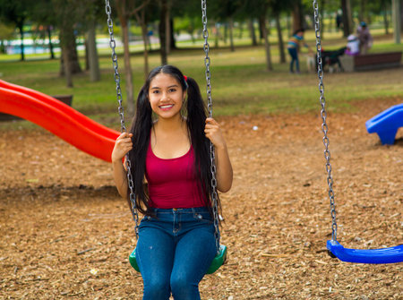 Young pretty teenage girl with pig tails wearing jeans and purple top, sitting on swing at outdoors...