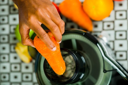 Closeup man's hands using juice maker, inserting carrot into machine, healthy lifestyle concept.の写真素材