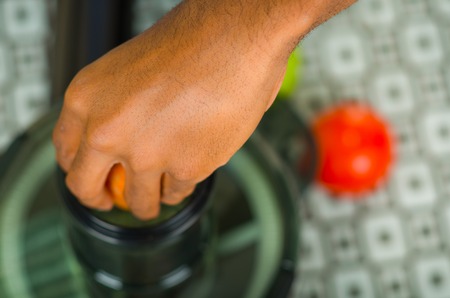 Closeup man's hands using juice maker, inserting carrot into machine, healthy lifestyle concept.の写真素材