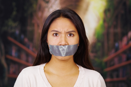 Young brunette woman wearing white sweater with and duct tape covering mouth, facing camera, hostage concept.の写真素材