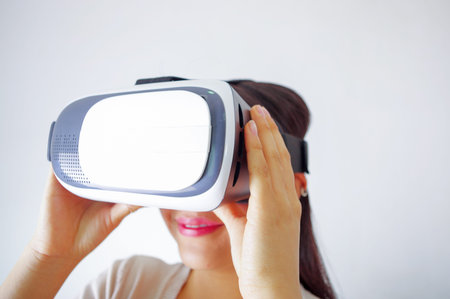 Young brunette woman wearing virtual reality goggles experiencing future technology, interacting and...