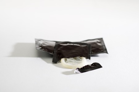 Closeup transparent condom as seen sticking out of the packaging lying on white surface, studio background, safe sex concept.の写真素材