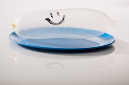 Closeup transparent condom filled with air lying on blue dinner plate, white studio background, safe sex concept.の写真素材