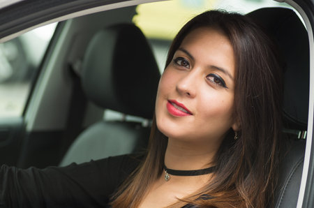 Closeup young woman sitting in car smiling to camera, as seen from outside drivers window, female...