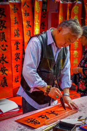 SHENZEN, CHINA - 29 JANUARY, 2017: Chinese man painting black letters on red banner, several banners hanging in background, chinese new year celebration conceptのeditorial素材