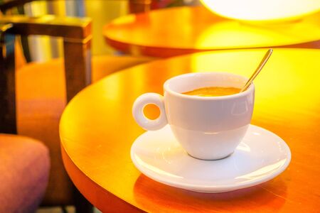Small white espresso cup sitting on saucer with coffee inside, cafeteria environmentの写真素材
