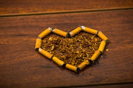 Cigarette butts shaped into a heart lying on wooden surface, tobacco spread around middle, seen from aboveの写真素材