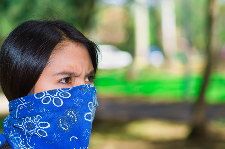 Young brunette woman wearing blue bandana covering half of face, interacting outdoors for camera, activist protest conceptの写真素材
