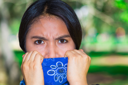 Young brunette woman wearing blue bandana covering half of face, interacting outdoors for camera, activist protest conceptの写真素材