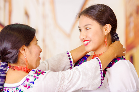 Beautiful portrait of mother with daughter, both wearing traditional andean clothes and matching necklaces, posing embracing happilyの写真素材
