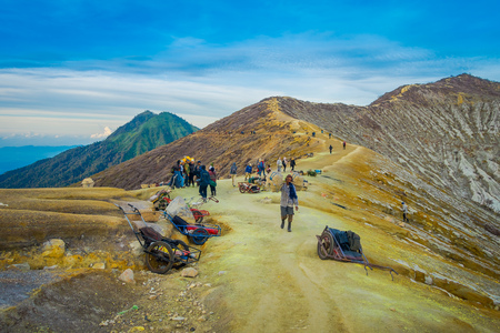 KAWEH IJEN, INDONESIA - 3 MARCH, 2017: Local miners carrying loads of yellow sulfur rocks up mountain side, tourist hiking attraction located inside volcanic crater, spectacular natureのeditorial素材