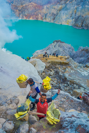KAWEH IJEN, INDONESIA - 3 MARCH, 2017: Local miners carrying heavy baskets of yellow sulfur rocks up mountain side, tourist hiking attraction located inside volcanic crater, spectacular natureのeditorial素材