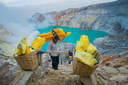 KAWEH IJEN, INDONESIA - 3 MARCH, 2017: Local miners carrying heavy baskets of yellow sulfur rocks up mountain side, tourist hiking attraction located inside volcanic crater, spectacular natureのeditorial素材