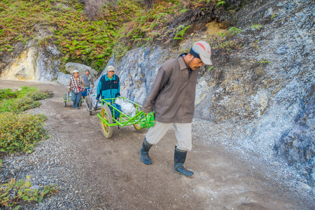 KAWEH IJEN, INDONESIA - 3 MARCH, 2017: Local miners using wheelbarrows to transport sulfur and equipment from mine located inside volcanic crater, high altitude landscapeのeditorial素材