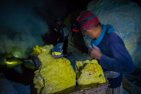 KAWEH IJEN, INDONESIA - 3 MARCH, 2017: Man wearing headlight working in sulfur mine, extracting yellow mineral rocks in dark environmentのeditorial素材