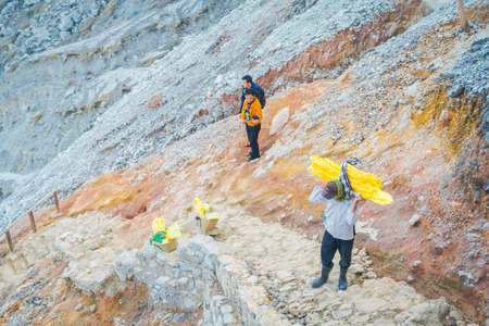 KAWEH IJEN, INDONESIA - 3 MARCH, 2017: Local miners carrying heavy loads of yellow sulfur rocks up mountain side, tourist hiking attraction located inside volcanic crater, spectacular natureのeditorial素材