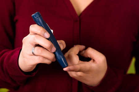 Woman with red sweater checking blood sugar level by glucometer and test stripe at homeの写真素材