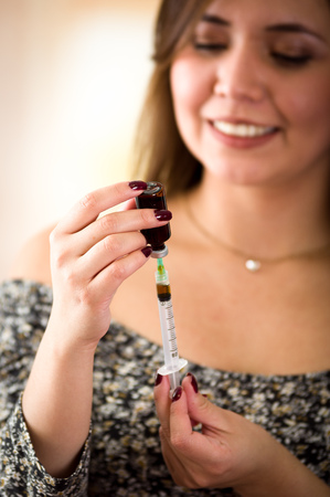 Beautiful young woman with syringe is preparing the substance to injectの写真素材