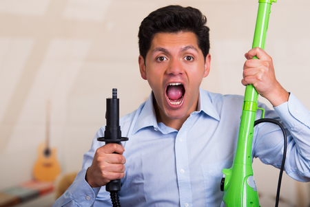 Handsome young Man holding a vacuum cleaner and screamingの写真素材