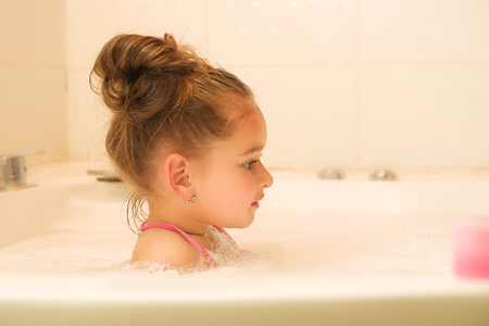 little beautiful girl playing with water and foam in bathの写真素材