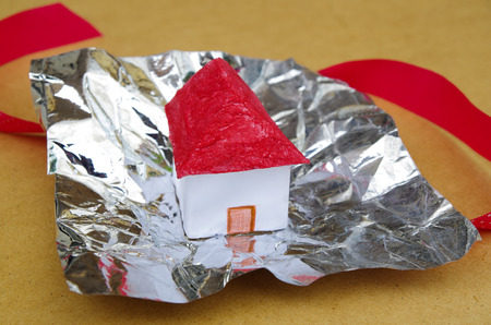 A small and beautiful house model concept over Aluminum foil with a red tie behindの写真素材
