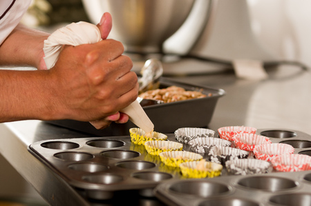 A bakery man is preparing a delicious christmas cookies in a bakery store, adding Dough inside of the cupcake Wrappersの写真素材