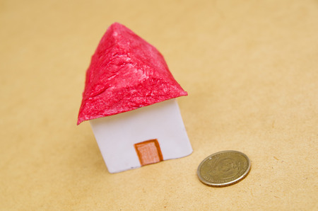 Small beautiful house with a coin in front of the housing model pretending: house prices, house buying, real estate, mortgage conceptの写真素材