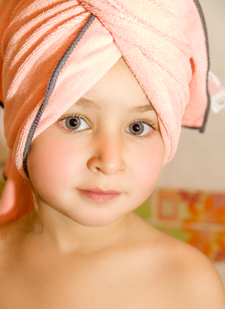 little beautiful girl with a bright eyes with a pink towel in her headの写真素材