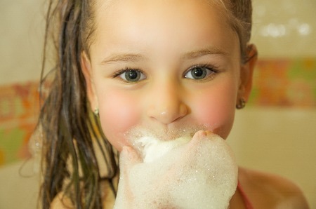 little beautiful girl playing with water and foam with her mouth in bathの写真素材