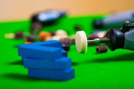 A gray drill with a small blue wooden pieces on a green background