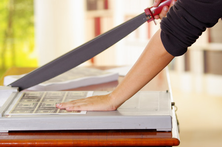 Man using manual paper cutter to cut the bills printed in the sheets of paper, on a wooden table, Manufacture workの写真素材
