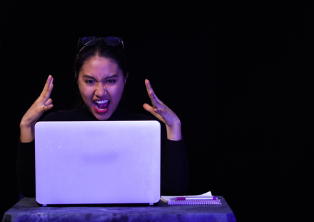 Beautiful girl screaming in front of her laptop on dark backgroundの写真素材