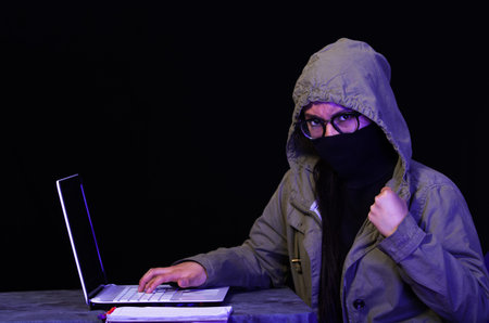 Portrait of a beautiful and smart girl hacker with laptop on dark background using glasses and...