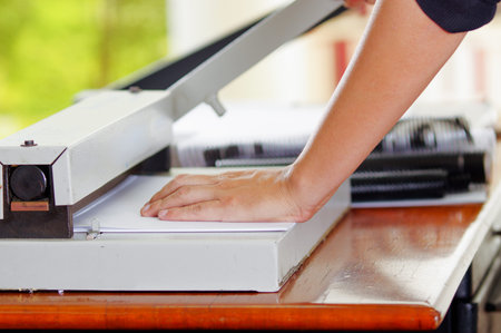 Man using manual paper cutter to cut the bills printed in the sheets of paper, on a wooden table,...