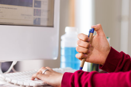 Close-up of a female hand holding a pen in a desk with a computer. fiddling concept
