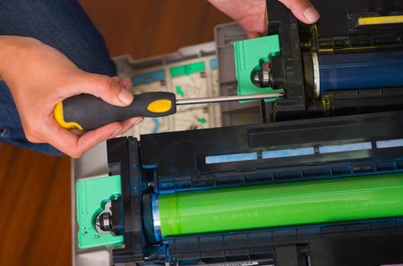 woman fixing a photocopier and smiling during maintenance using a screwdriver
