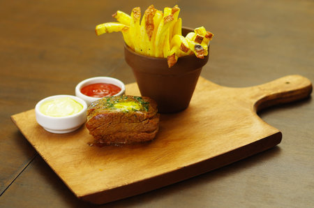 Well-done grilled marinated beef flank steak with ketchup, mustard and french fries on wooden boardの写真素材